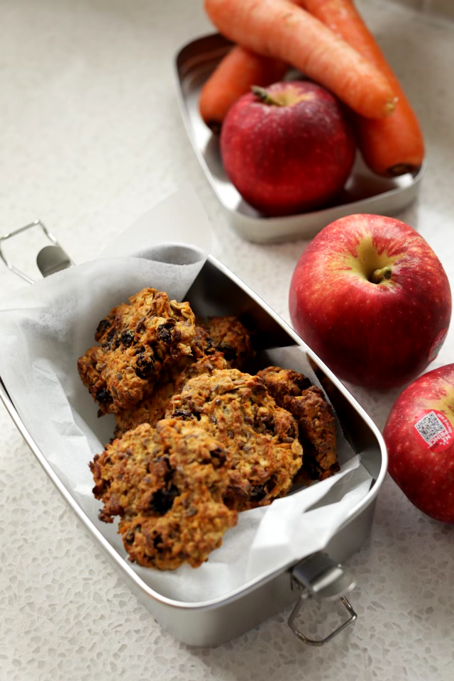Fruit and vege cookies inside stainless steel lunchbox beside apples and carrots