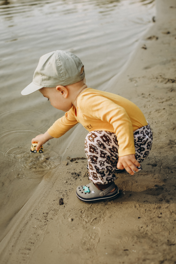Child wearing a yellow top standing on the beach playing with a truck in the ocean