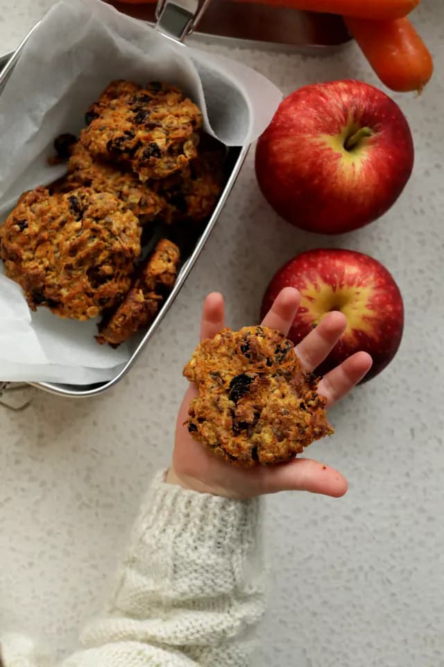 Fruit and vege cookies in todder's hand with ingredients and cookies in the background