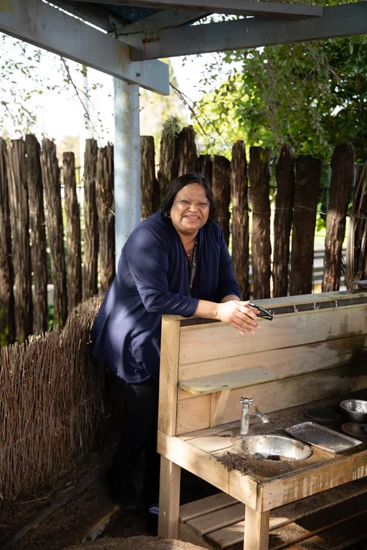 Lady smiling standing leaning arms against wooden bench