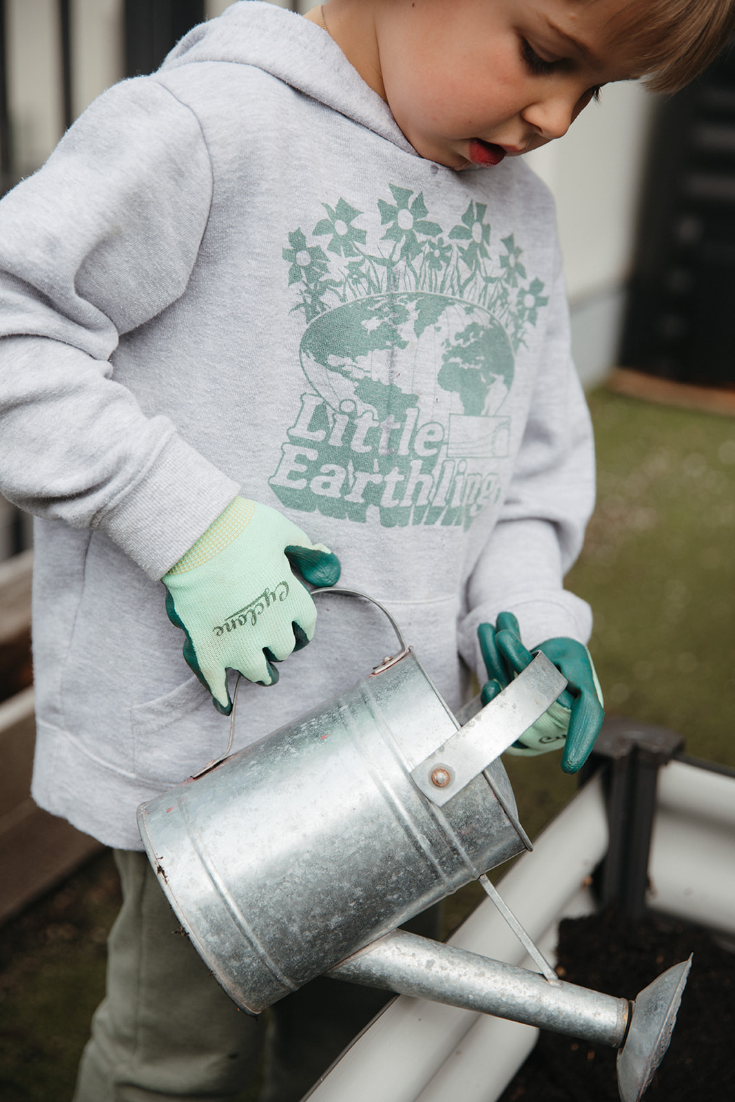 Toddler wearing gardening gloves using watering can